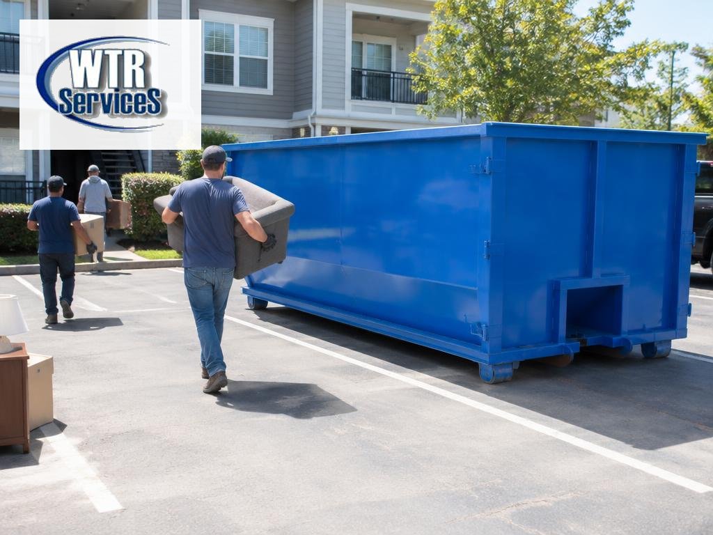 WTR Services guide to property management dumpster rental showing workers carrying furniture toward a blue roll-off dumpster at an apartment complex